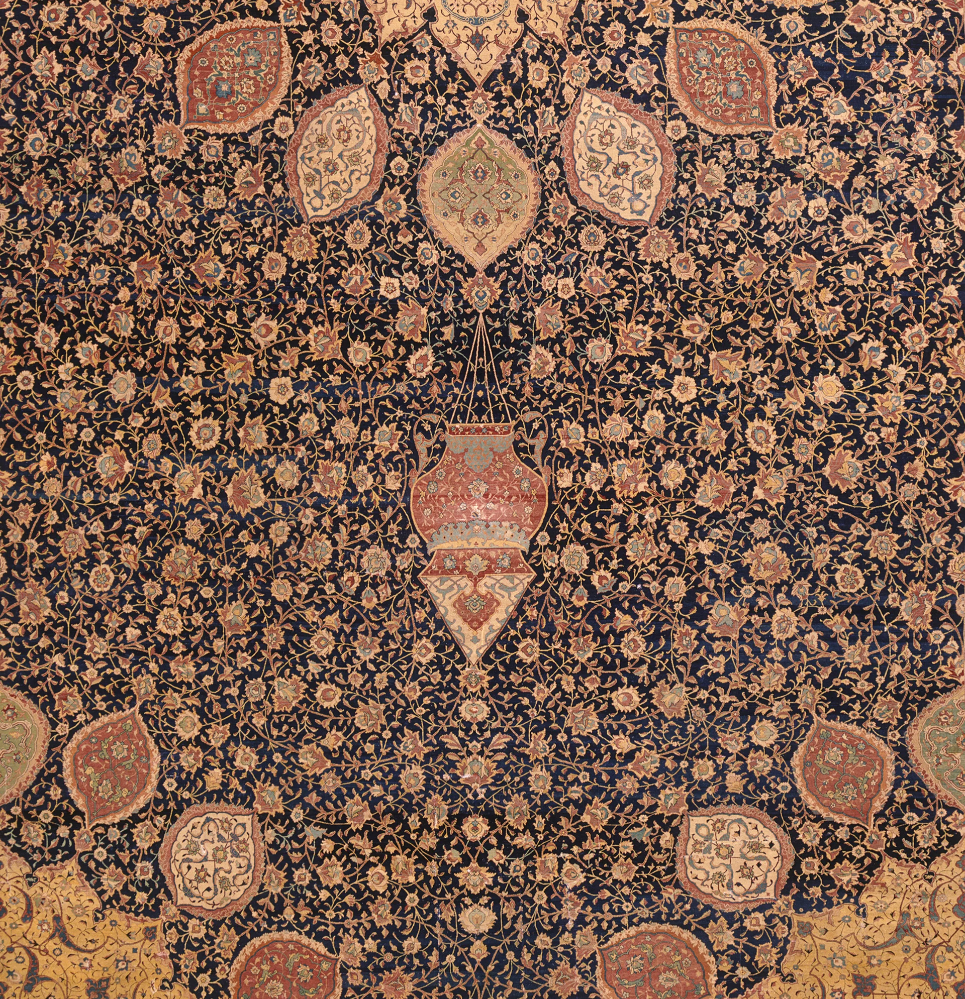 Detail of carpet focused on ornate hanging lamp surrounded by floral patterns in black, gold, and red.